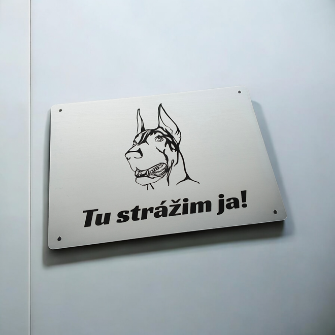 Strieborná tabuľka s hlavou dobermana a nápisom Tu strážim ja